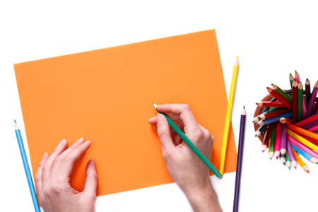 Human hands with pencil drawing something on the orange paper isolated on white background. Painting. Artist. Education and school.の写真素材