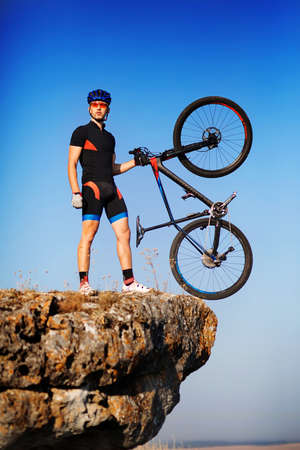 Man biker holding bike on the top of a hill against beautiful blue sky.の写真素材