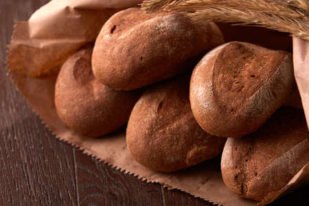 loafs of brown bread, packaged in a paper bag on wooden background