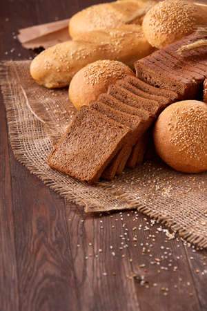 Assortement of bread on burlap on the wooden table. Slices of bread and roll.の写真素材
