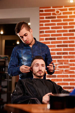 Master combing hair of men in the barbershop, hairdresser makes hairstyle for a young manの写真素材