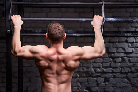 Young attractive caucasian crossfit sportsman working out in gym, rear view