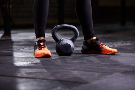 Cropped image of young woman, legs in the black leggings, orange sneakers and kettlebell. Crossfit workoutの写真素材
