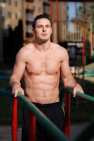 Portrait of fit and happy young sportsman leaning on wall bars at the park