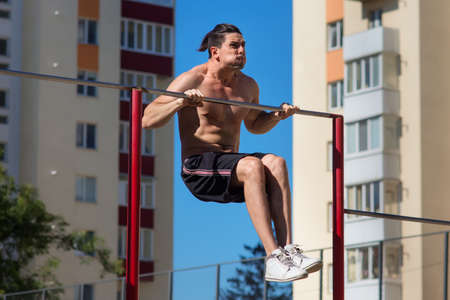 Fit young man doing push ups on horizontal bar outdoors with big effort.の写真素材