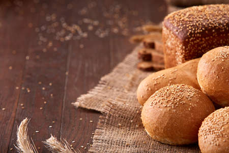 Different bread on burlap on the wooden table close-up. With wheat and ears of wheat. Slices of the brown bread. Rulls and baguette.の写真素材