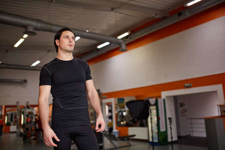 Muscular young athletic built sportsman standing against hall of the gym