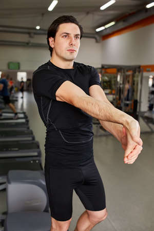 Sporty man in the black sportwear stretching arms before gym workout.