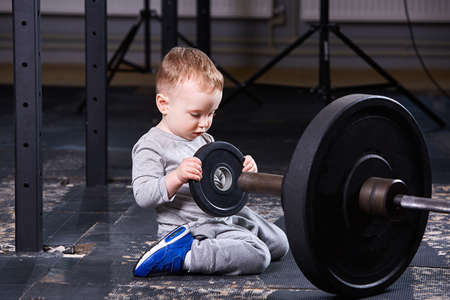 Little cute child in sportwear in the cross fit gym with a barbell.の写真素材