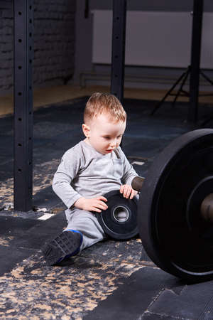 Little cute child in sportwear in the cross fit gym with a barbell.の写真素材