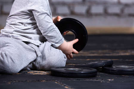 Close-up photo of little boy with barbell against brick wall in the cross fit gym.の写真素材