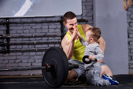Portrait of happy father and son with barbell in the cross fit gym against brick wall.の写真素材