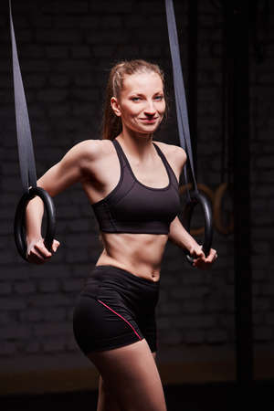 Fit young sporty woman holding gymnast rings and smiling at the cross fit gym against brick wall.の写真素材