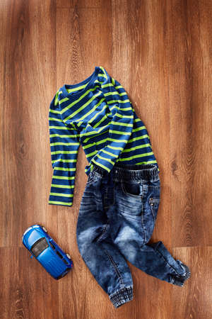 Childrens jacket and jeans with blue toy car on a wooden background.の写真素材