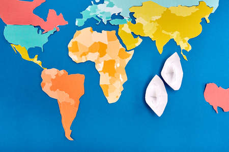 World map cut out of colored paper and two white paper ship based on blue.の写真素材