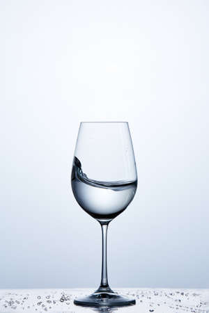 Pure water wave in the wine glass while standing on the glass with drapes against light background.の写真素材