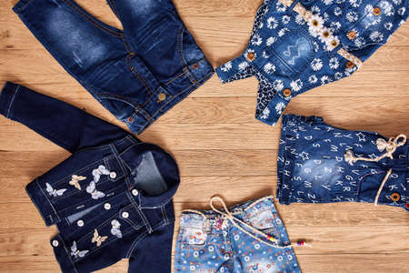 Childrens jeans, jacket, denim shorts and denim dress on wooden background.