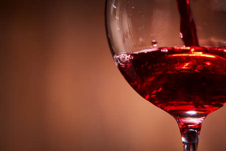 Close-up of brightly red wine poured in the wineglass and abstract splashing against brown background.の写真素材