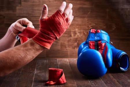 Sportive man wrapping his hands with bandage and boxing gloves on wooden plank.の写真素材