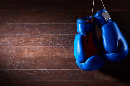 A pair of bright blue and red boxing gloves hangs against wooden background.の写真素材