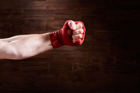 Boxer fist punch with red bandage on a wooden background.