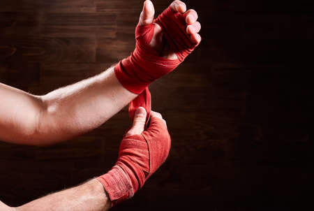 Boxer putting bandage around wrists and hands against brown wall.の写真素材