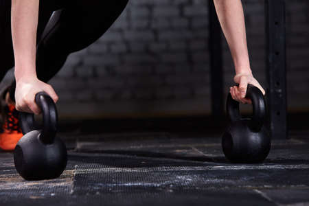 Close-up photo of young athlete womans hands while doing push ups on kettlebells against brick wall in the gym.の写真素材