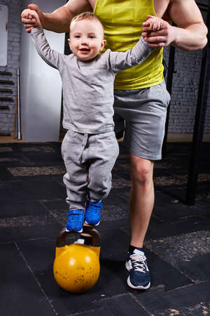 Happy father and little cute son exercising with dumbbells and smiling while against brick wall.の写真素材