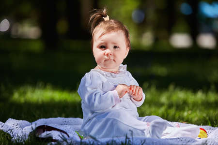 Baby girl in summer dress sitting in the green meadow in the city park.の写真素材