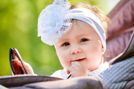 Close-up of the funny baby girl sitting in the stroller and holds sunglasses.の写真素材