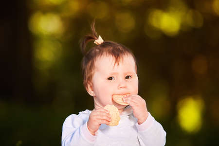 Close-up of cute baby girl sitting in the park and eats the snack at warm day.の写真素材