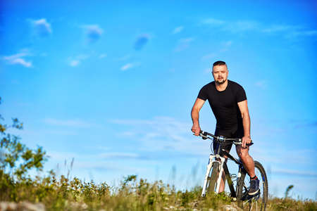 Young man cycling on a green meadow against blue sky with clouds.の写真素材