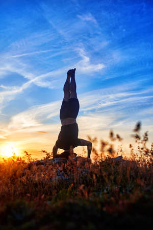 Young man practicing yoga and stretching on a rock at sunset light.