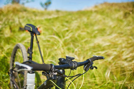 Close-up of detail of the mountain bicycle on the green grass. Helm and wheel of the bicycle. Horizontal photo. Sportive backgrounds. Extreme travelling in the countryside. Concept of the healthy and active lifestyle.の写真素材