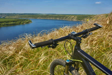 Close-up of helm of the mountain bicycle in the green grass against beautiful landscape. Detail of the bicycle and nature. Horizontal photo. Extreme travel in the countryside. Sporty backgrounds. Concept of the healthy lifestyle.の写真素材