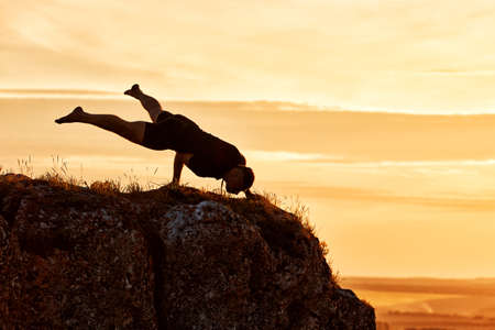 Silhouette of man doing yoga meditation against beautiful sky with clouds. Horizontal photo of young sportsman and beautiful lnadscape with sunset. Practicing yoga in the countryside. Concept of the healthy and active lifestyle.の写真素材