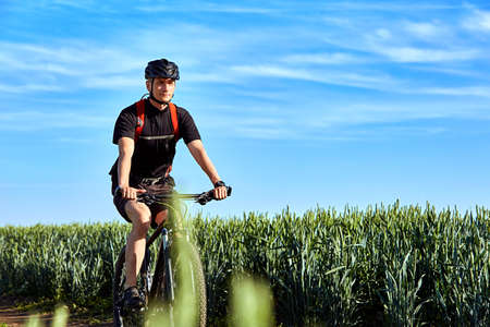 Attractive cyclist rides on the road in a field on a bright sunny day against blue sky.の写真素材