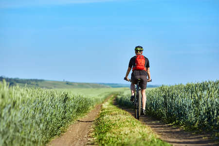 Rear view of the young cyclist with backpack cycling in the track of the field.の写真素材