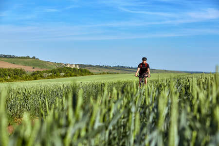 Attractive cyclist rides on the road in a field on a bright sunny day against blue sky.の写真素材
