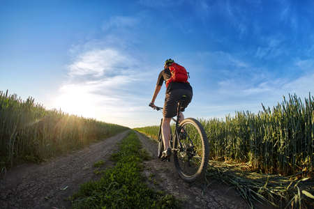 Cyclist in the helmet riding mountain bicyclist on outdoor trail against sunrise.