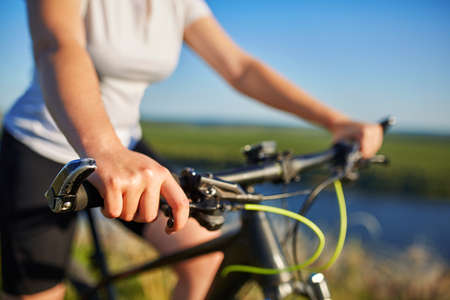 young slender woman sitting on bicycle, holding handlebars with hands. Woman in the park sunset lighting.の写真素材