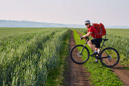 Young cyclist riding bicycle on the road on green field.の写真素材