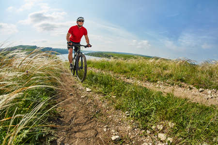 Young cyclist riding mountain bicycle through green meadow against beautiful sky.