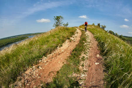 Young cyclist riding mountain bicycle through green meadow against beautiful sky.