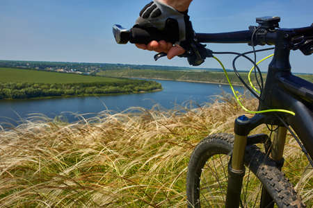 Close-up of the cyclist holding bicycle on the meadow in the countryside against beautiful landscape.の写真素材