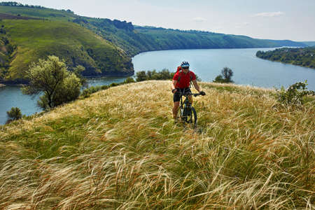 Attractive cyclist riding mountainbike on the meadow above river in summer season in the countryside.の写真素材