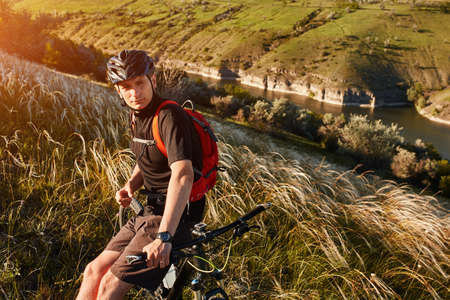 Attractive cyclist rirding mountain bike above beautiful river in the field in the countryside.の写真素材
