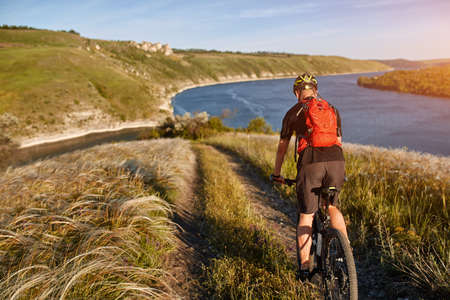 Attractive cyclist rirding mountain bike above beautiful river in the field in the countryside.の写真素材