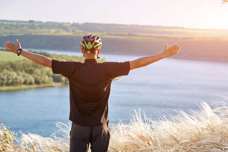 Portrait of the young cyclist standing on the hill above the river against blue sky with clouds.の写真素材