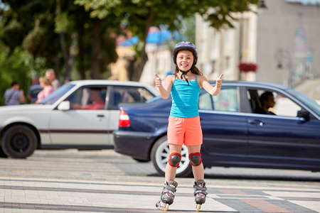 Funny Little pretty girl on roller skates in helmet riding in a park.の写真素材
